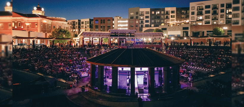 The Bowl amphitheater at Sugar Hill, GA at night, with a packed crowd and the mixed-use downtown development lit up behind it